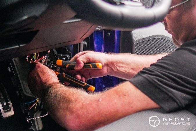 Ghost Installations engineer working on the wiring under a car dashboard